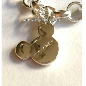 Puede incluir: Pulsera de plata con un dije en forma de cabeza de Mickey Mouse. El dije es de plata y tiene la palabra "Disney" grabada.