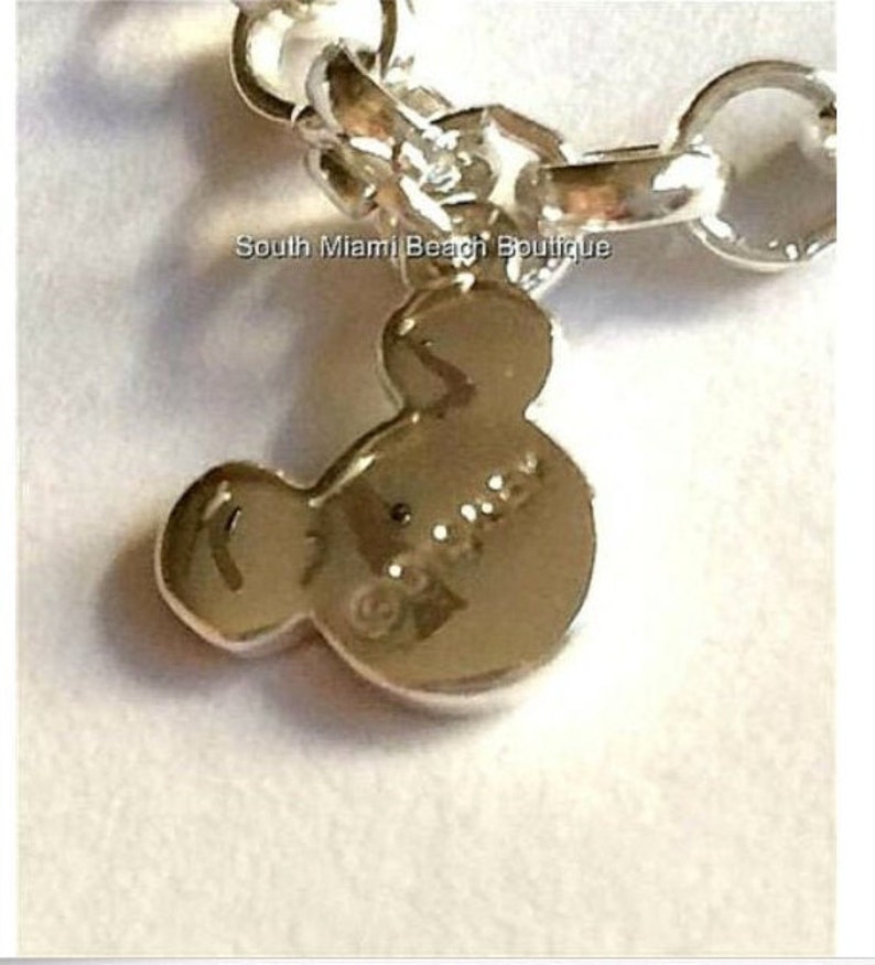 Puede incluir: Pulsera de plata con un dije en forma de cabeza de Mickey Mouse. El dije es de plata y tiene la palabra "Disney" grabada.