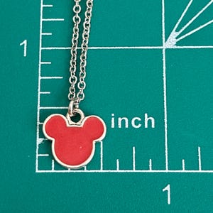 K&ouml;nnte beinhalten: Eine silberne Kettenkette mit einem roten Mickey Mouse Kopf-Anh&auml;nger. Der Anh&auml;nger ist etwa 2,5 cm gro&szlig;.
