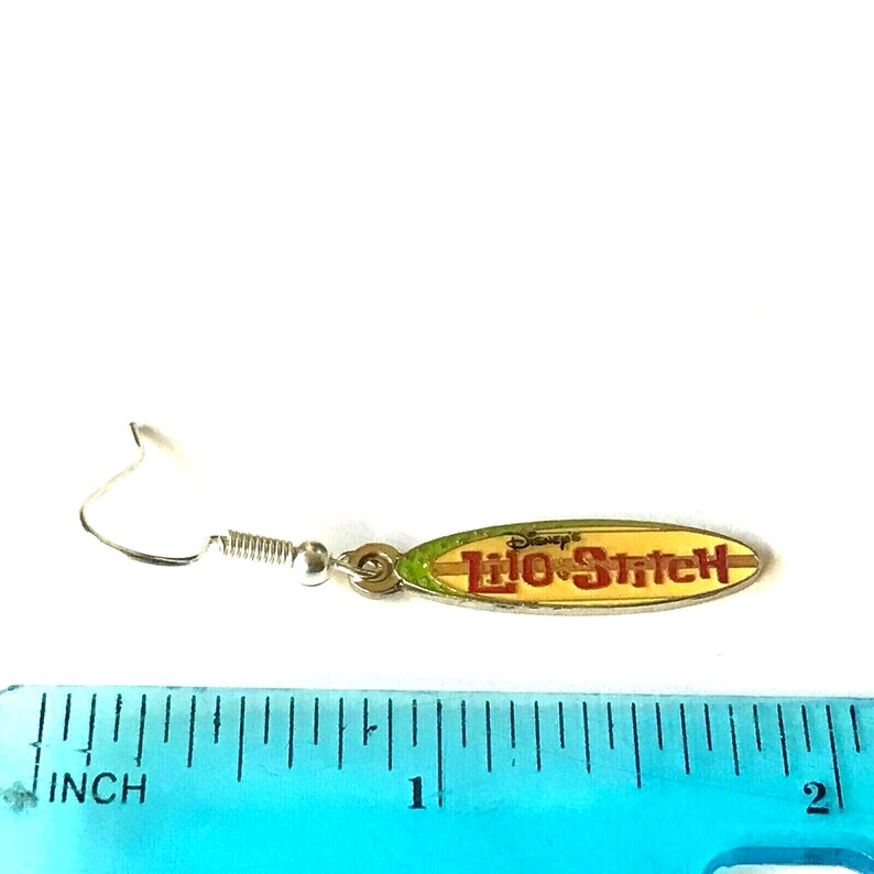 May include: Silver Lilo & Stitch surfboard earrings with a yellow, green, and red design. The earrings are about 1 inch long.
