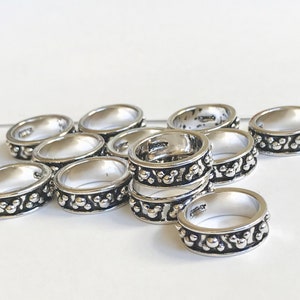 Puede incluir: Una colecci&oacute;n de anillos plateados con un dise&ntilde;o detallado. Cada anillo presenta una banda de peque&ntilde;os patrones circulares en relieve en los bordes. Los anillos se exhiben sobre una superficie blanca, mostrando su apariencia pulida.