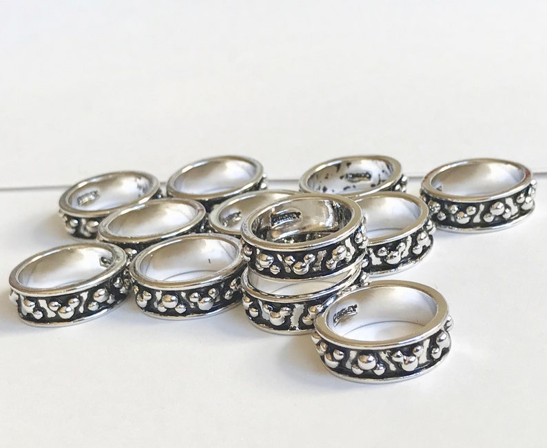 Puede incluir: Una colecci&oacute;n de anillos plateados con un dise&ntilde;o detallado. Cada anillo presenta una banda de peque&ntilde;os patrones circulares en relieve en los bordes. Los anillos se exhiben sobre una superficie blanca, mostrando su apariencia pulida.