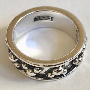 Puede incluir: Un anillo plateado con una banda de peque&ntilde;as cuentas redondas en relieve. El anillo tiene un acabado pulido y un interior liso. La palabra "Disney" est&aacute; estampada dentro del anillo.