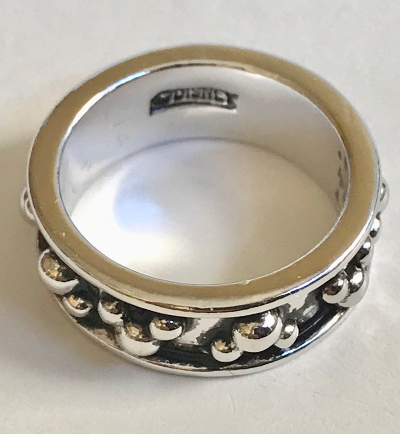 Puede incluir: Un anillo plateado con una banda de peque&ntilde;as cuentas redondas en relieve. El anillo tiene un acabado pulido y un interior liso. La palabra "Disney" est&aacute; estampada dentro del anillo.