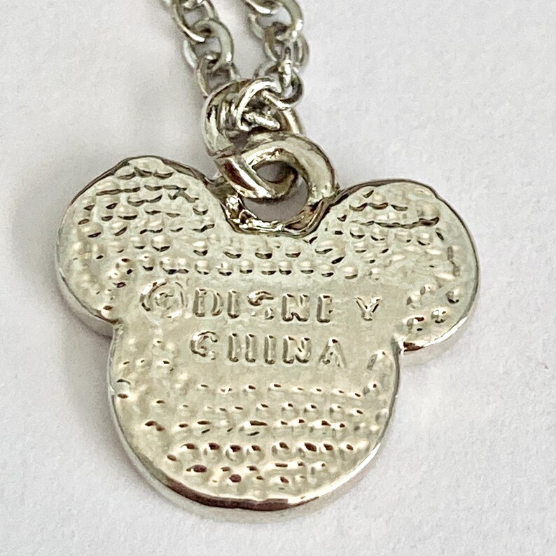 K&ouml;nnte beinhalten: Silberne Halskette mit einem Anh&auml;nger in Form eines Mickey Mouse Kopfes. Auf der R&uuml;ckseite des Anh&auml;ngers ist der Text "Disney China" eingraviert.