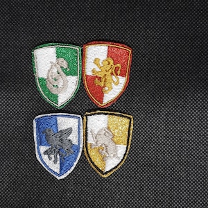 Op de afbeelding: Vier geborduurde schildpatches met de emblemen van de Hogwarts-huizen. De patches bevatten een groene en zilveren slang, een rode en gouden leeuw, een blauwe en zilveren adelaar en een gele en zilveren das. Elke patch heeft een witte rand.