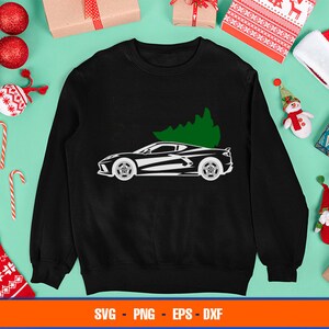 May include: A black sweatshirt with a white silhouette of a sports car with a Christmas tree on top. The sweatshirt is surrounded by Christmas decorations.