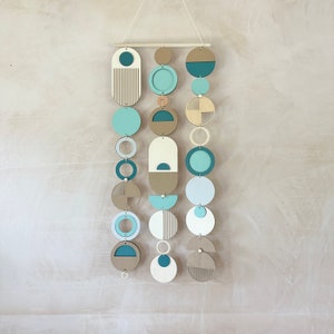 A handmade large wall hanging made of plywood and other materials. Measuring 80cm long by 32cm wide. Painted mainly in blue, green and yellow tones. Inspired by the colours you see at a beach.
