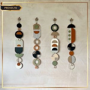 Può includere: Tre pezzi di arredamento da parete sospesi con forme geometriche in nero, bianco, verde, marrone e beige. Ogni pezzo presenta una combinazione di cerchi, semicerchi e rettangoli.