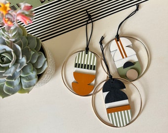 May include: Three wooden ornaments with geometric designs in black, white, green, and orange. Each ornament is attached to a gold ring.