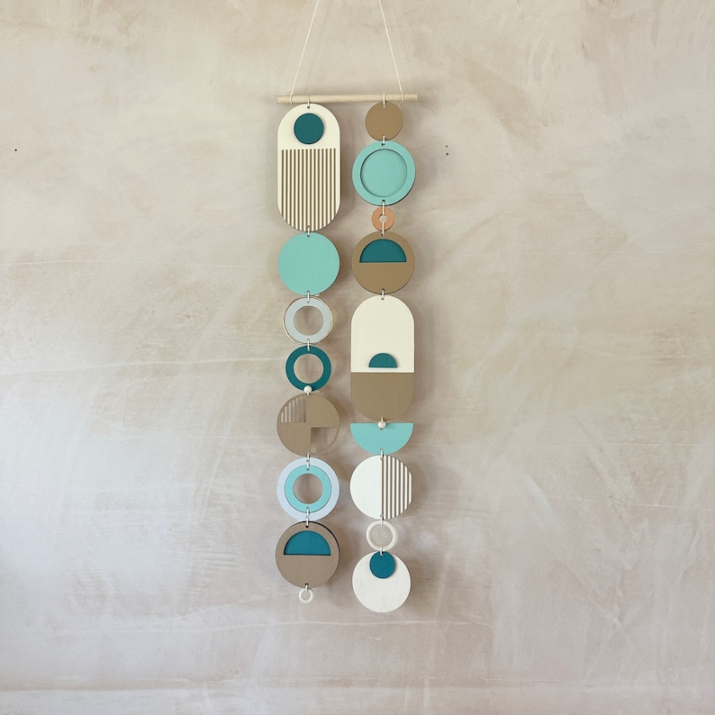 A handmade large wall hanging made of plywood and other materials. Measuring 80cm long by 22cm wide. Painted mainly in blue, green and yellow tones. Inspired by the colours you see at a beach.