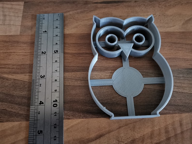 Pu&ograve; includere: Un tagliabiscotti a forma di gufo in plastica grigia con un righello accanto. Il tagliabiscotti &egrave; alto circa 10 cm. Il righello mostra le misure in pollici. Il tagliabiscotti ha un corpo circolare con un design a croce.