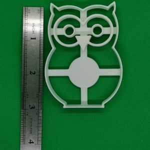 Pu&ograve; includere: Un tagliabiscotti a forma di gufo in plastica bianca con un righello accanto. Il tagliabiscotti &egrave; alto circa 10 cm. Il design del gufo presenta grandi occhi, un becco e un corpo rotondo. Lo sfondo &egrave; di colore verde.