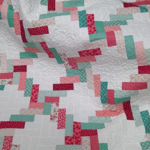 May include: A quilt featuring a white background with a repeating pattern of rectangular fabric strips in shades of teal, light pink, and dark pink. The white fabric sections are quilted with a swirling, continuous line stitch pattern throughout.