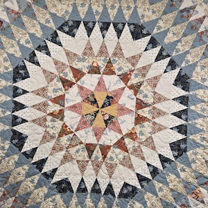 May include: A quilt featuring a complex star pattern composed of numerous triangular fabric pieces. The design incorporates a variety of floral and geometric prints in shades of blue, cream, pink, yellow, and dark brown, with visible quilting stitches.