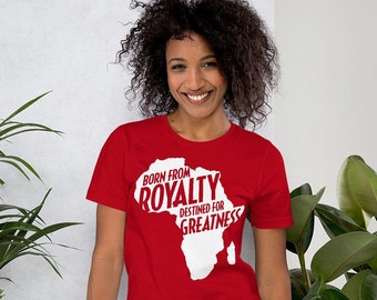 Puede incluir: Camiseta roja de manga corta con un contorno blanco del continente africano. El texto "Born from Royalty Destined for Greatness" está escrito en el contorno de África.