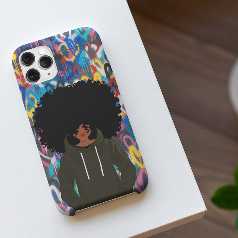 Puede incluir: Una funda de tel&eacute;fono con un fondo de graffiti colorido que presenta a una mujer con un afro y una sudadera verde. El graffiti incluye corazones y otras formas abstractas.