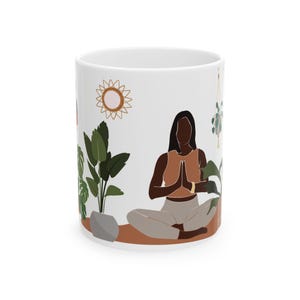 Pu&ograve; includere: Tazza in ceramica bianca con una donna dalla pelle scura che medita con le mani in posizione di preghiera. La donna indossa una canotta marrone e pantaloni grigi. La tazza presenta anche un sole, una pianta sospesa e una pianta in vaso.