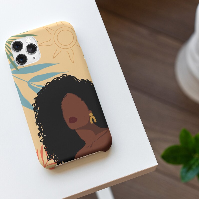 May include: A phone case with a colorful illustration of a woman with curly hair, a sun, and tropical leaves. The background is a light yellow color.