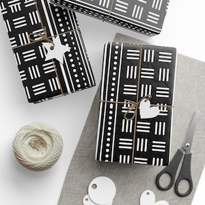 Könnte beinhalten: Drei schwarz-weiße Geschenkboxen mit weißen Bändern und Papieretiketten. Die Boxen sind in verschiedenen Mustern verpackt, darunter ein geometrisches Muster, ein gestreiftes Muster und ein Tupfenmuster.