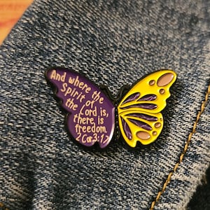 May include: Purple and yellow enamel pin shaped like a butterfly with the text "And where the Spirit of the Lord is, there is freedom. 2 Cor. 3:17"