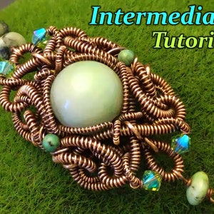 Könnte beinhalten: Ein Anhänger aus umwickeltem Kupferdraht mit einem grünen Stein und schillernden Kristallen. Der Anhänger befindet sich auf einem grünen Hintergrund mit dem Text "Intermediate Tutorial".