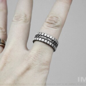 Op de afbeelding: Een zilveren ring met een geometrisch ontwerp van afwisselende zwarte en zilveren vierkanten.