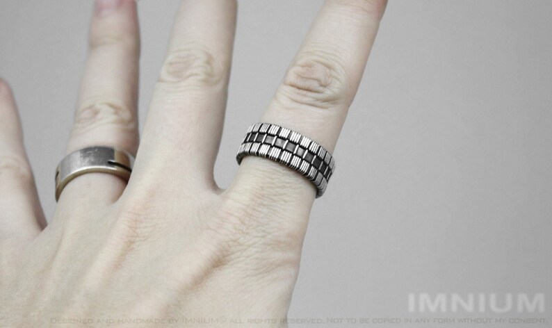 Op de afbeelding: Een zilveren ring met een geometrisch ontwerp van afwisselende zwarte en zilveren vierkanten.