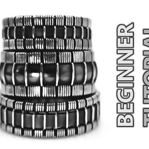 Op de afbeelding: Een stapel van vijf zilveren en zwarte armbanden met een geometrisch patroon. De armbanden zijn op elkaar gestapeld en verticaal gerangschikt. De armbanden zijn gemaakt van metaal en hebben een glanzende afwerking. De achtergrond is wit. BEGINNERSHANDLEIDING