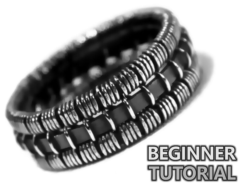 Op de afbeelding: Een zilveren en zwarte ring met een geweven ontwerp. De ring is gemaakt van meerdere banden van metaal en zwart materiaal.