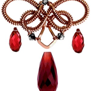 Op de afbeelding: Een hanger van koperdraad met een geknoopt ontwerp en drie rode druppelvormige kristallen.