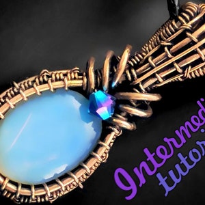 Op de afbeelding: Een hanger omwikkeld met koperdraad met een lichtblauwe ovale steen en een klein iriserend blauw kristal. De hanger is bevestigd aan een koperen draadbeugel. De afbeelding bevat de tekst "Intermediate Tutorial".