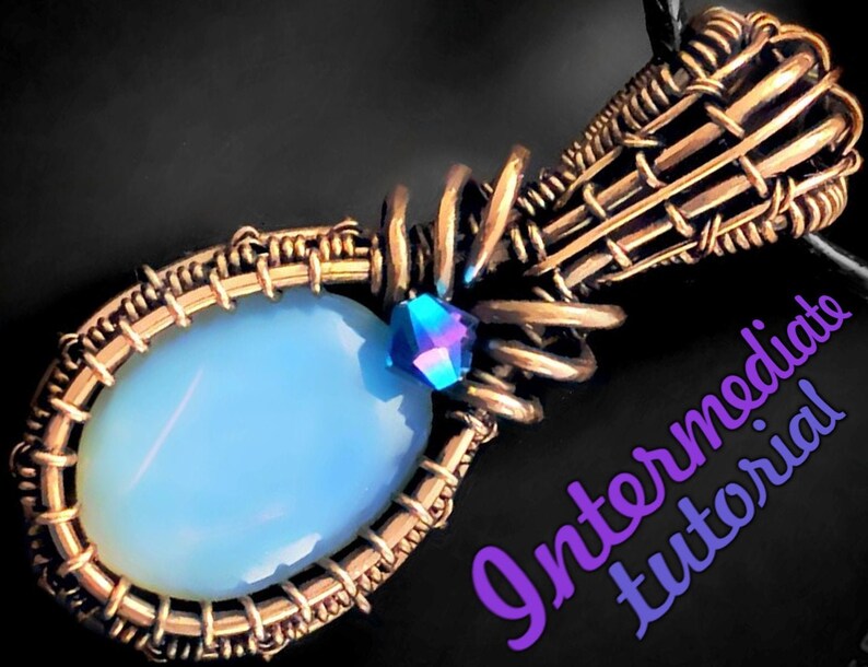 Op de afbeelding: Een hanger omwikkeld met koperdraad met een lichtblauwe ovale steen en een klein iriserend blauw kristal. De hanger is bevestigd aan een koperen draadbeugel. De afbeelding bevat de tekst "Intermediate Tutorial".