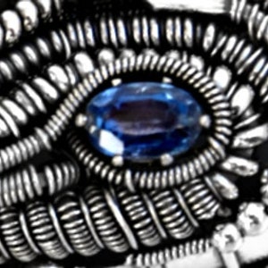 Peut inclure: Gros plan sur une bague en fil d'argent avec une pierre pr&eacute;cieuse bleue au centre.