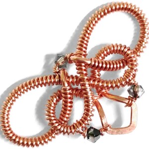 Op de afbeelding: Een sculptuur van koperdraad met een delicaat, ingewikkeld ontwerp. De sculptuur heeft meerdere lussen en draaiingen, waardoor een uniek en opvallend stuk ontstaat. De sculptuur is versierd met kleine, heldere kristallen.