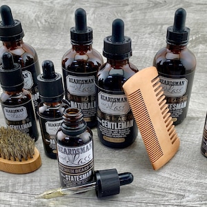 May include: A collection of seven amber glass bottles with droppers, each labeled "BEARDSMAN and LASS" with different beard oil scents. The scents include "Statesman", "Gentleman", "Naturalist", and "Natural".  A wooden comb and a wooden brush are also included.