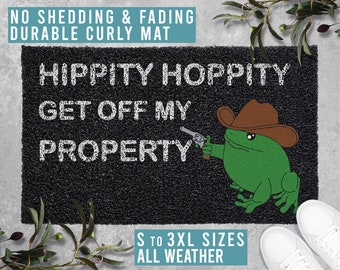 May include: A black doormat with white text that reads "Hippity Hoppity Get Off My Property". A cartoon frog wearing a cowboy hat and holding a gun is on the doormat. The doormat is made of durable curly material and is available in sizes S to 3XL.