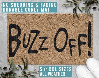 Puede incluir: Una alfombra de coco marrón con el texto "Buzz Off!" en letras negras. La alfombra se anuncia como "No Shedding & Fading Durable Curly Mat" y "S to XXL Sizes All Weather".