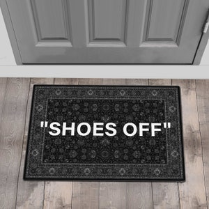 Może przedstawiać: Czarna wycieraczka z ozdobnym obramowaniem i napisem "SHOES OFF" białymi literami.