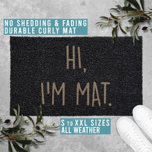 Puede incluir: Felpudo negro con el texto "HI, I'M MAT." en letras beige. El felpudo está hecho de fibras rizadas y tiene el texto "S TO XXL SIZES ALL WEATHER" impreso debajo del texto principal.