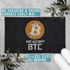 May include: Black doormat with a white curly texture. The doormat has a large orange Bitcoin symbol and the text "WE ACCEPT BTC" in white. The doormat also has the text "S TO XXL SIZES ALL WEATHER" in white.