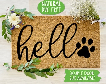 May include: A brown coir doormat with the text "hello" in black cursive lettering and a black paw print. The doormat is surrounded by green leaves and white flowers. The text "NATURAL PVC FREE" is in a green circle above the doormat. The text "DOUBLE DOOR SIZE AVAILABLE" is in a green rectangle below the doormat.