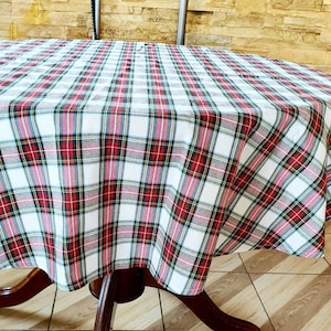May include: A white tablecloth with a red, green, and yellow plaid pattern. The tablecloth is draped over a round wooden table.