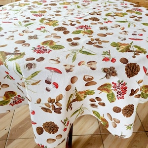 May include: White round tablecloth with a brown, red and green autumnal pattern featuring mushrooms, acorns, leaves and pine cones.