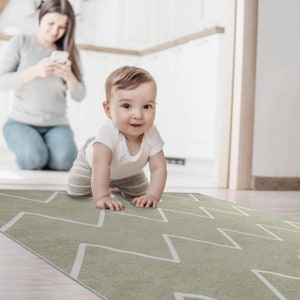 May include: A baby in a white onesie crawls on a green and white chevron patterned play mat.