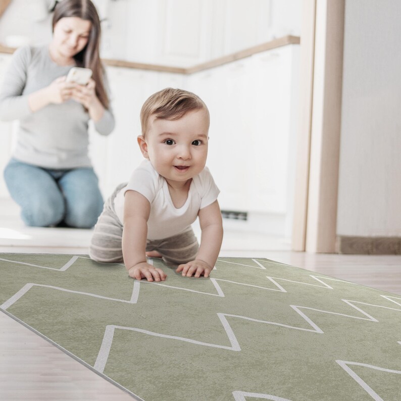 May include: A baby in a white onesie crawls on a green and white chevron patterned play mat.