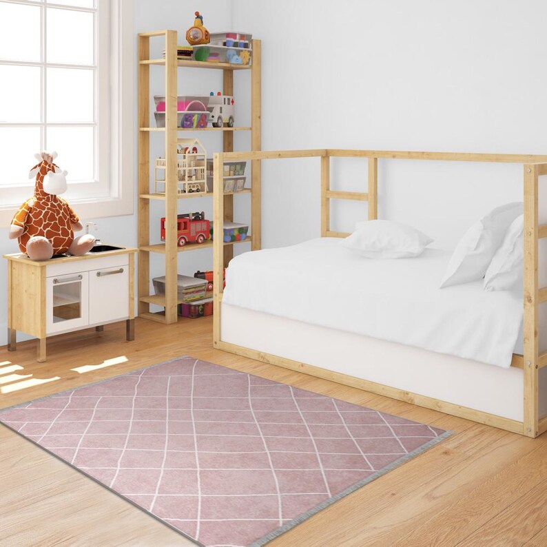 May include: A pink and white diamond patterned rug with a gray border. The rug is in a child's bedroom with a wooden bed and a bookshelf filled with toys.