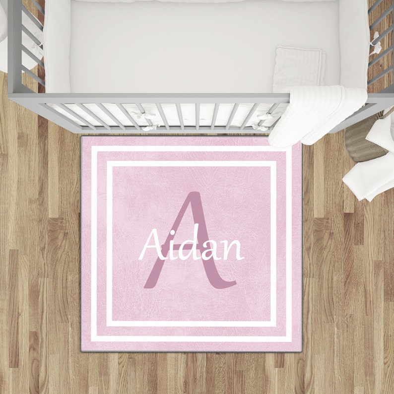 May include: Pink personalized nursery rug with a white border and the name "Aidan" in white lettering. The letter "A" is in a larger font and is pink.