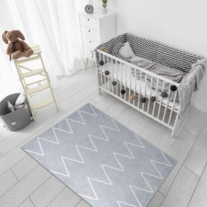 May include: A gray and white chevron patterned rug in a nursery with a white crib and a white wooden step stool.