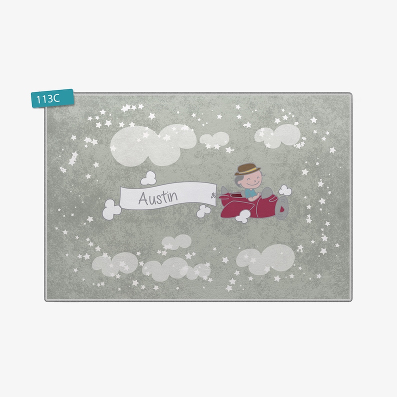 May include: A light gray rug with a white background featuring a cartoon illustration of a boy flying a red airplane with a banner that says "Austin" in white letters. The background is filled with white stars and clouds.